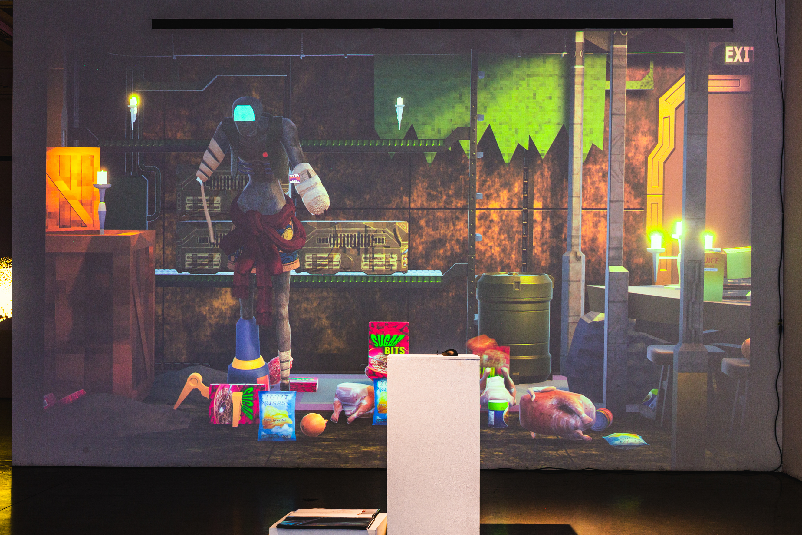 A projection onto a white wall of a computer animation game, where a humanoid figure stands in a rustic metal room. In front of the projection is a white podium with a computer mouse.